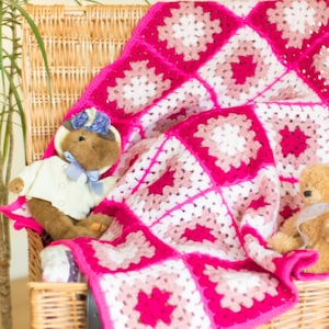 May include: A pink, white and brown crocheted blanket with a granny square pattern. Two teddy bears are sitting on a wicker chair with the blanket draped over them.