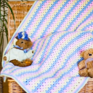 May include: Two teddy bears are sitting on a wicker basket lined with a crocheted blanket. The blanket is made with pink, blue, and yellow yarn in a striped pattern.