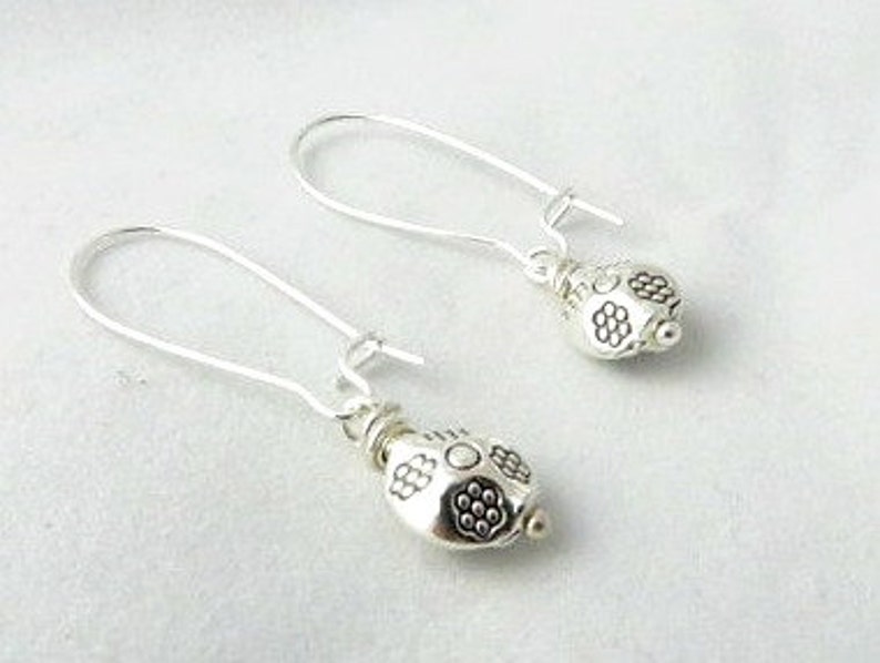 May include: A pair of silver dangle earrings with a small, round, textured bead at the end of each earring.