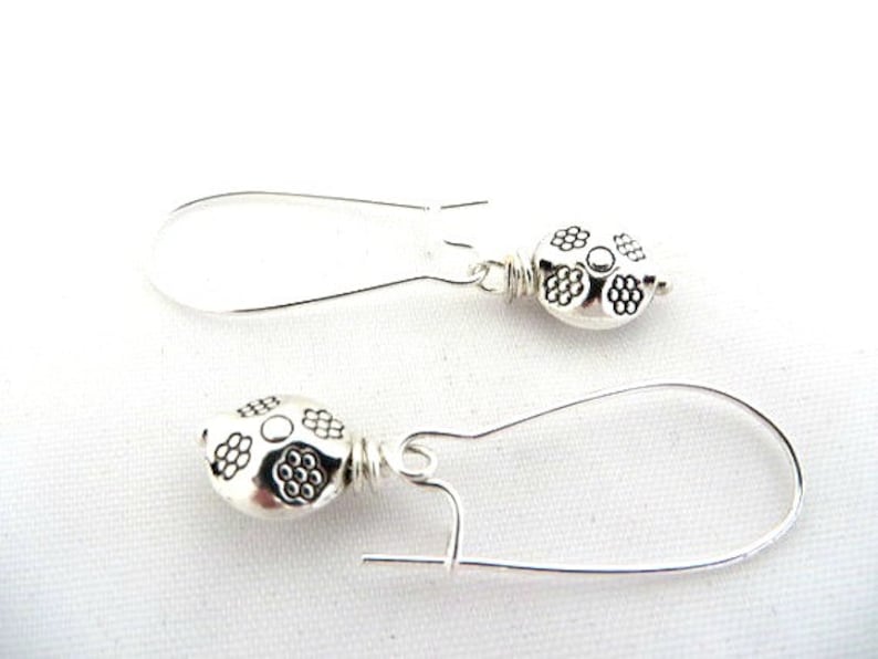May include: A pair of silver earrings featuring a floral design. The earrings are made from silver wire and have a small, round, silver charm with a floral pattern.