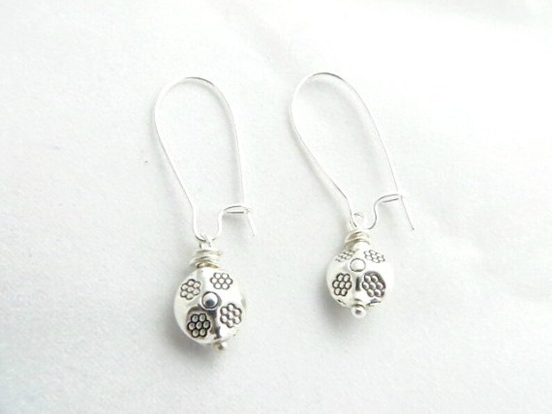 May include: A pair of silver dangle earrings with a round, textured bead at the end of each earring.