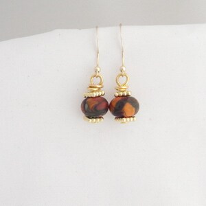 May include: A pair of dangle earrings with a brown and orange marbled bead on each earring. The beads are accented with gold-colored metal.