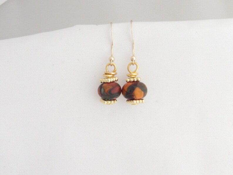 May include: A pair of dangle earrings with a brown and orange marbled bead on each earring. The beads are accented with gold-colored metal.