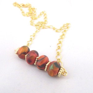 May include: A gold chain necklace with four orange, black, and green patterned beads.