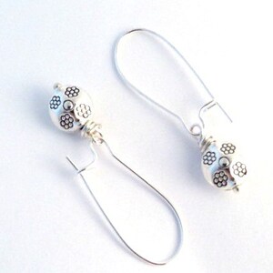 May include: Silver dangle earrings with a round, textured bead featuring a floral design.