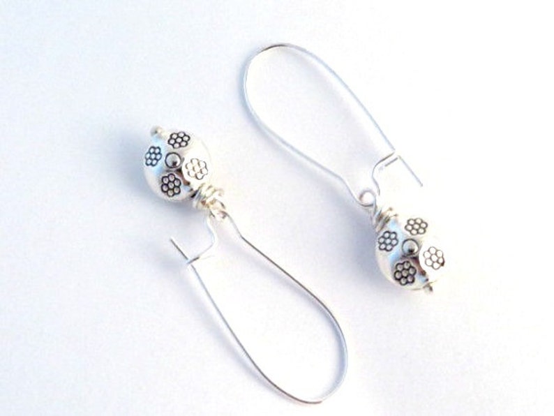 May include: Silver dangle earrings with a round, textured bead featuring a floral design.