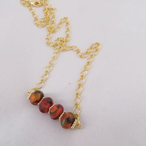 May include: A gold chain necklace with a short strand of red, orange, and black patterned beads.