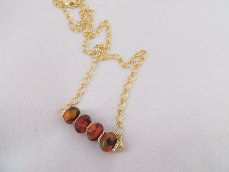 May include: A gold chain necklace with a short strand of red, orange, and black patterned beads.