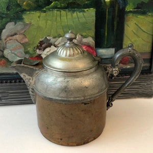 May include: A silver and copper teapot with a lid and a handle. The teapot has a decorative design around the top and bottom.