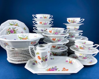 May include: A set of white porcelain dinnerware with a floral pattern in shades of pink, orange, and yellow. The set includes plates, bowls, cups, and saucers.