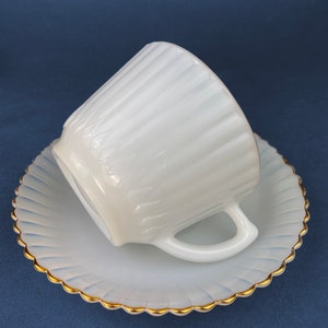 May include: White milk glass teacup and saucer set with a gold rim. The cup and saucer have a fluted design.