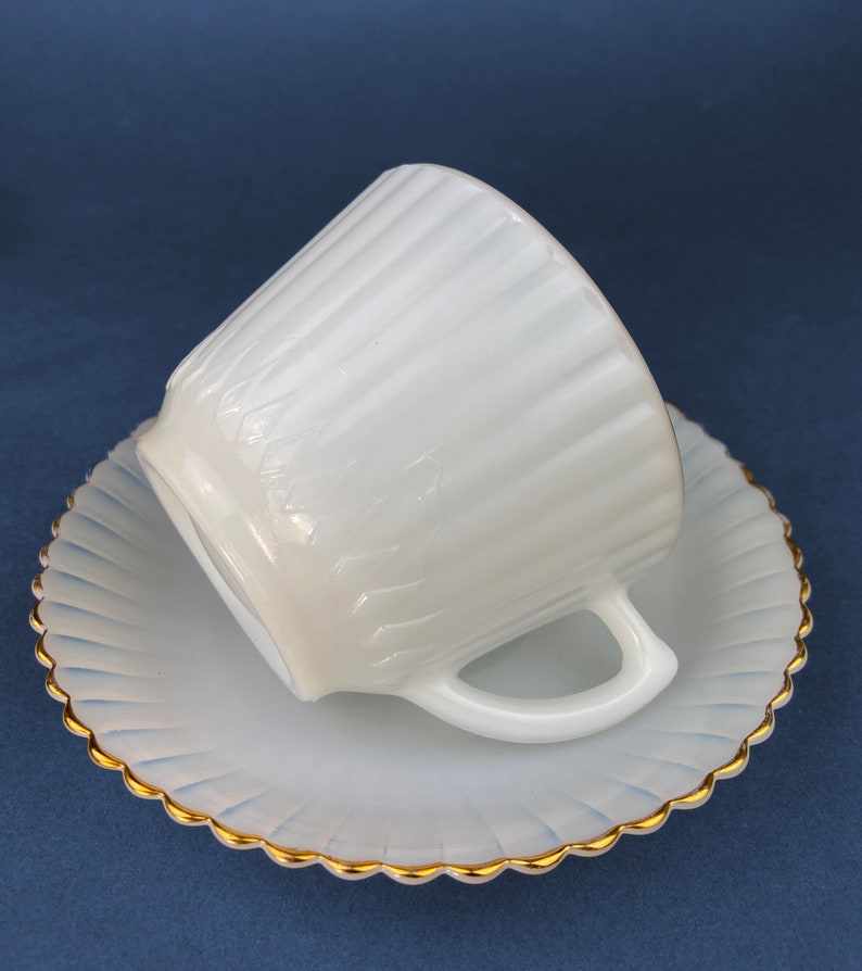 May include: White milk glass teacup and saucer set with a gold rim. The cup and saucer have a fluted design.
