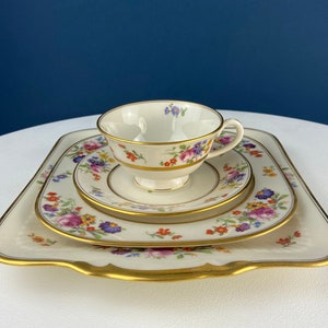 May include: A set of three white porcelain plates with a gold rim and a floral pattern. The plates are nested together, with the smallest plate on top. The plates are decorated with a variety of colorful flowers, including pink, purple, and yellow.