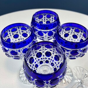 Puede incluir: Cuatro vasos con tallo de cristal transparente y azul cobalto con un patr&oacute;n geom&eacute;trico. Los vasos est&aacute;n dispuestos en c&iacute;rculo sobre una superficie blanca.