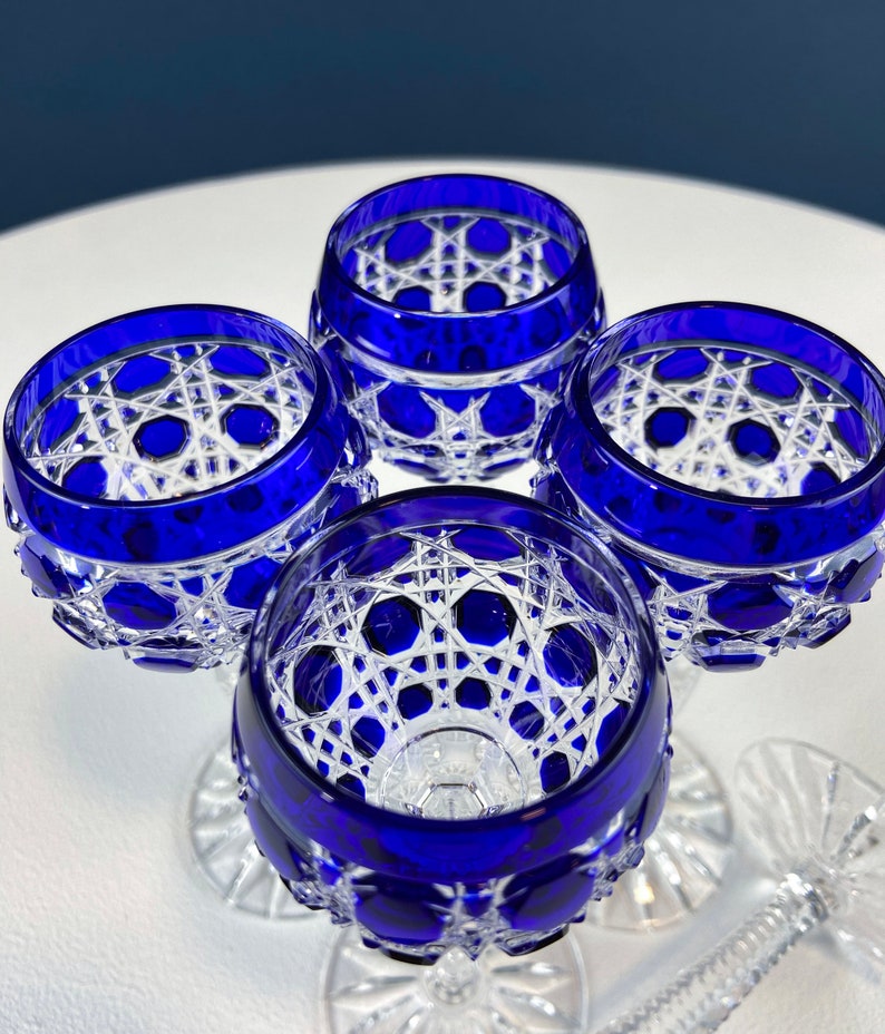 Puede incluir: Cuatro vasos con tallo de cristal transparente y azul cobalto con un patr&oacute;n geom&eacute;trico. Los vasos est&aacute;n dispuestos en c&iacute;rculo sobre una superficie blanca.