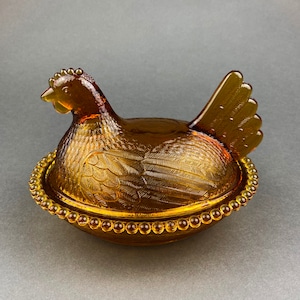 Glazen kip op nest. Goudgeel gekleurde glazen kip in een mand.  Trinketschaal met deksel. Zeer verzamelbaar.  Cadeau voor hem of haar.