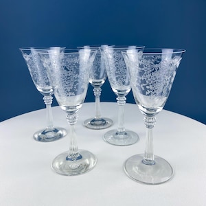 Puede incluir: Conjunto de cinco copas de vino de vidrio transparente con un diseño floral grabado. Las copas tienen un tallo alto y delgado y una copa ancha.