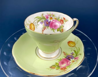 May include: A vintage teacup and saucer set with a delicate floral design. The cup and saucer are a pale green color with a gold trim. The floral design features pink, yellow, and purple flowers.
