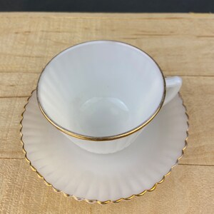 May include: White teacup and saucer with a gold rim. The saucer has a scalloped edge.