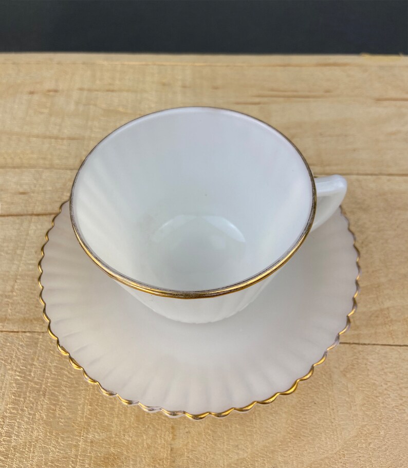 May include: White teacup and saucer with a gold rim. The saucer has a scalloped edge.