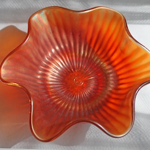 May include: A vintage orange glass bowl with a ruffled edge and a swirl pattern. The bowl has a iridescent finish.