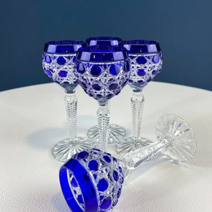 Puede incluir: Juego de cuatro copas de cristal tallado con tallo, de color azul cobalto, con intrincados dise&ntilde;os. Las copas est&aacute;n dispuestas sobre una superficie blanca.