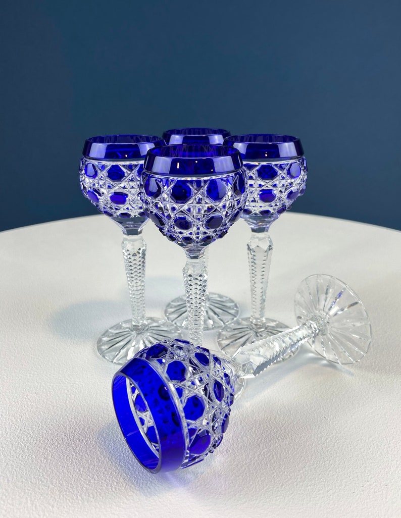 Puede incluir: Juego de cuatro copas de cristal tallado con tallo, de color azul cobalto, con intrincados dise&ntilde;os. Las copas est&aacute;n dispuestas sobre una superficie blanca.