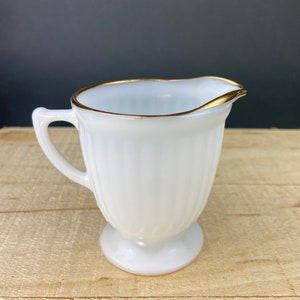 May include: White milk glass creamer with a gold rim. The creamer has a fluted design and a pedestal base.