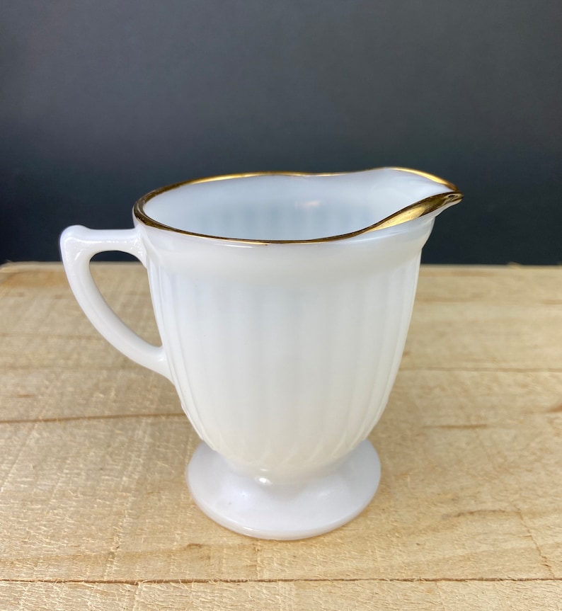 May include: White milk glass creamer with a gold rim. The creamer has a fluted design and a pedestal base.