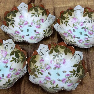 May include: Set of five white porcelain bowls with a floral design. The bowls have a scalloped edge and are decorated with pink roses, green leaves, and brown accents.