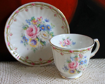 Puede incluir: Una taza de té y un platillo blancos con un patrón floral. La taza y el platillo tienen un borde dorado y presentan un delicado diseño floral con flores rosas, azules y amarillas.