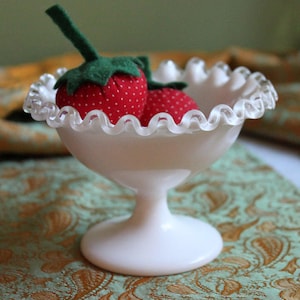 以下が含まれることがあります： フリルのある縁取りが施された白いミルクガラスの台座ボウルに、赤と白の布製のイチゴが2つ入っています。