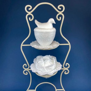 May include: White milk glass bird and cabbage dish set on a white metal stand. The bird dish has a bird with a nest design. The cabbage dish has a cabbage design. The stand has a scrolled design.