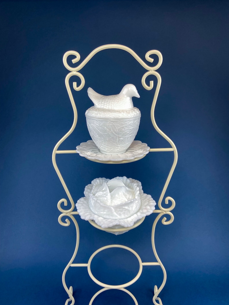 May include: White milk glass bird and cabbage dish set on a white metal stand. The bird dish has a bird with a nest design. The cabbage dish has a cabbage design. The stand has a scrolled design.
