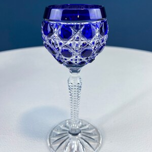 Puede incluir: Una copa de cristal tallado de color azul cobalto con tallo. La copa tiene una copa redonda y un tallo alto y delgado.