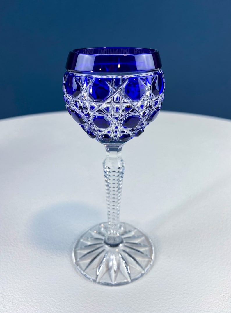Puede incluir: Una copa de cristal tallado de color azul cobalto con tallo. La copa tiene una copa redonda y un tallo alto y delgado.