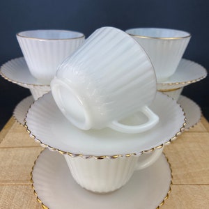 May include: A set of six white milk glass teacups and saucers with a gold rim. The cups and saucers have a fluted design.