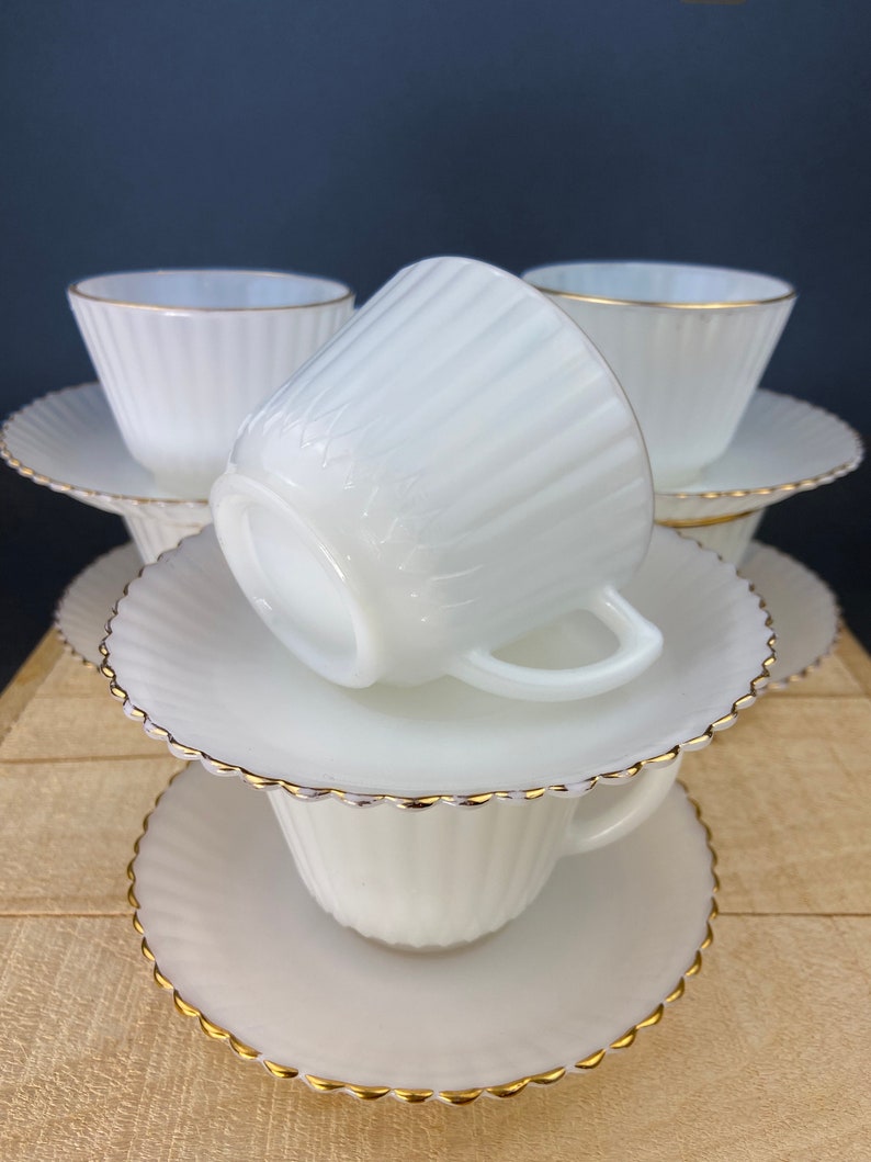 May include: A set of six white milk glass teacups and saucers with a gold rim. The cups and saucers have a fluted design.