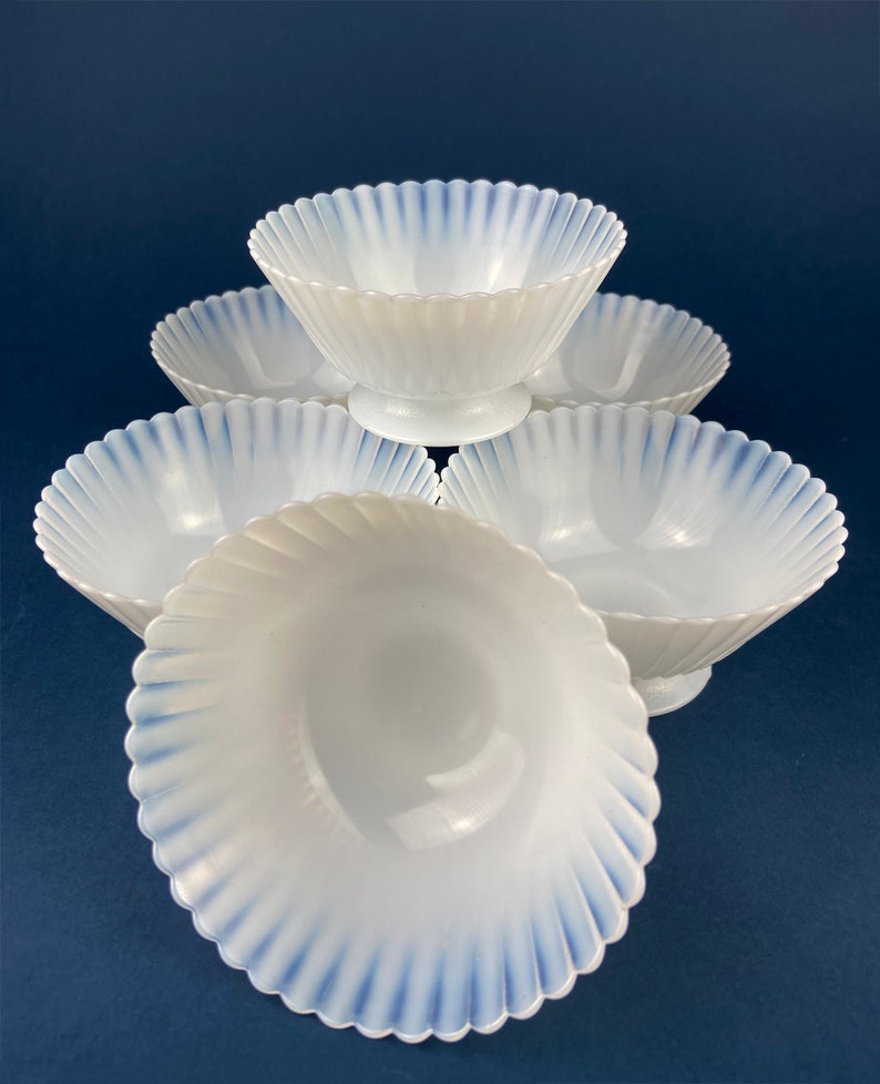 May include: Set of six white opalescent glass bowls with blue trim. The bowls have a scalloped edge and a fluted design.
