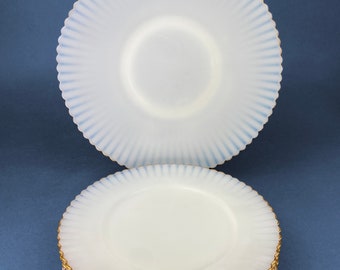 May include: A stack of eight white milk glass plates with a scalloped edge and a gold rim. The plates have a fluted design.