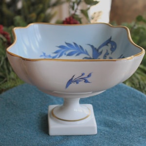 Op de afbeelding: Een witte keramische kom met een blauw en gouden bloemenmotief. De kom staat op een voet.