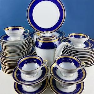 Puede incluir: Juego de té de porcelana en blanco y azul, con detalles dorados. El juego incluye tazas, platillos, platos y una tetera. Los platos y tazas están apilados ordenadamente. Un diseño clásico para la hora del té.