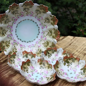 May include: A set of four white porcelain bowls with a floral design. The bowls have a scalloped edge and are decorated with pink roses, green leaves, and brown accents.