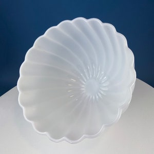 May include: A white, swirl-patterned glass bowl with a scalloped rim. The bowl is empty and appears to be made of opaque glass.