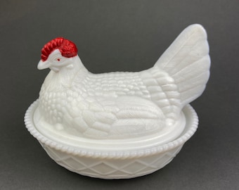 May include: White milk glass chicken butter dish with a red comb. The chicken is sitting in a nest with a woven pattern.