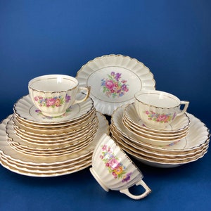 Puede incluir: Un juego de vajilla de porcelana blanca vintage con un patrón floral. El juego incluye una taza de té, un platillo y varios platos.