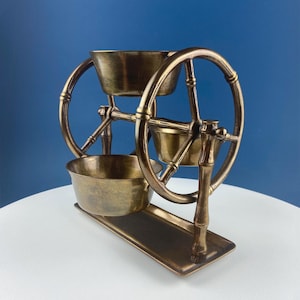 Peut inclure: Un support décoratif en laiton avec trois bols et un motif de roue. Le support est conçu pour ressembler à un petit chariot à roues.