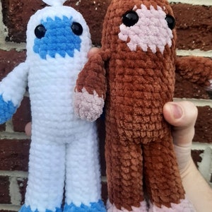 Puede incluir: Dos juguetes de peluche tejidos a crochet. Uno es blanco con detalles azules y el otro es marrón con detalles rosas.