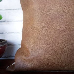 May include: A brown leather pillow with a textured surface.