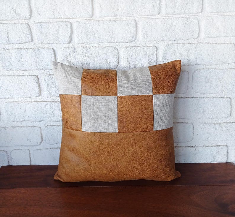 May include: A brown and beige checkered throw pillow with a faux leather bottom. The pillow is made of a soft, textured fabric.